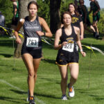 Elodie Wilson runs with a member of the host team at Cherokee’s meet.